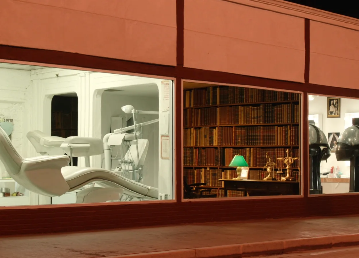 A night street of local businesses: a dental office, a law office, and a hair salon, each lit behind its shopfront window.